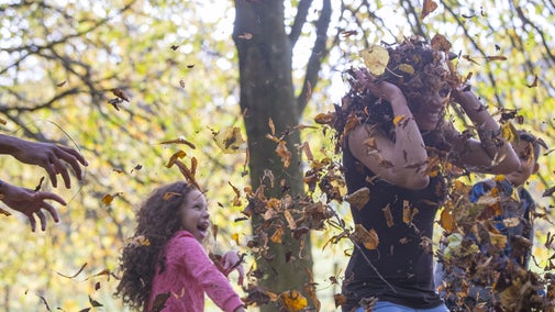 Little girl throwing fallen leaves on her mum